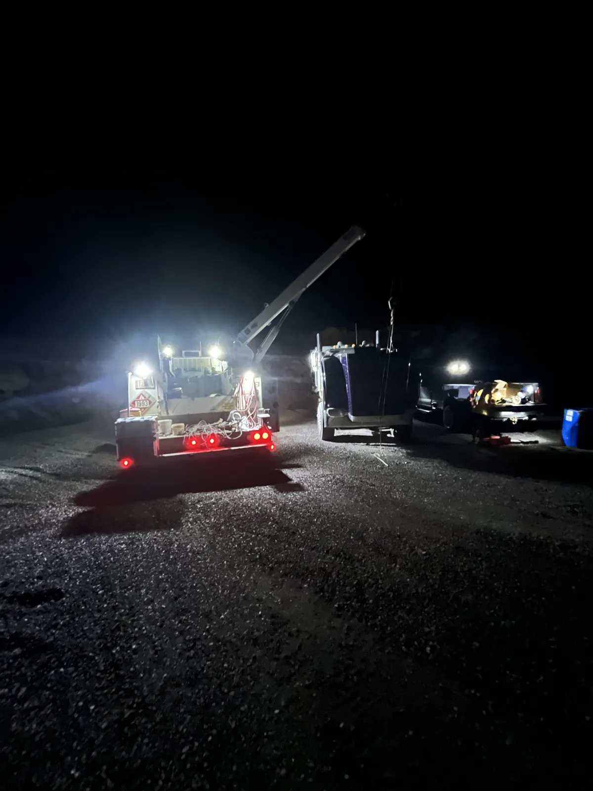 Trucks and equipment illuminated by work lights at night.